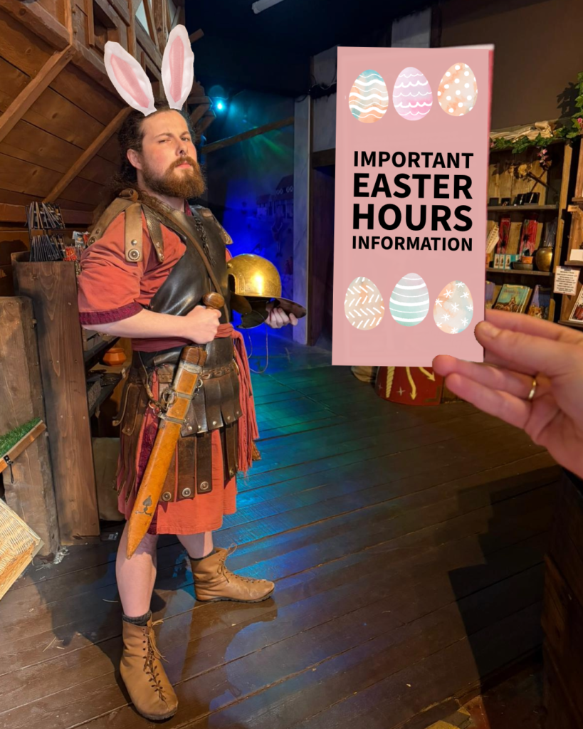 A bearded man, dressed as a Roman solider, inside a wooden area, with dramatic lighting. Someone is holding up a piece of paper. Digitally added are rabbit ear's on the man's head and a sign over the paper that says Important Easter Hours Information.